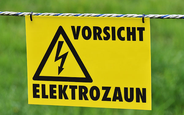 Warnschild "Vorsicht Elektrozaun" hängt im Leitermaterial.