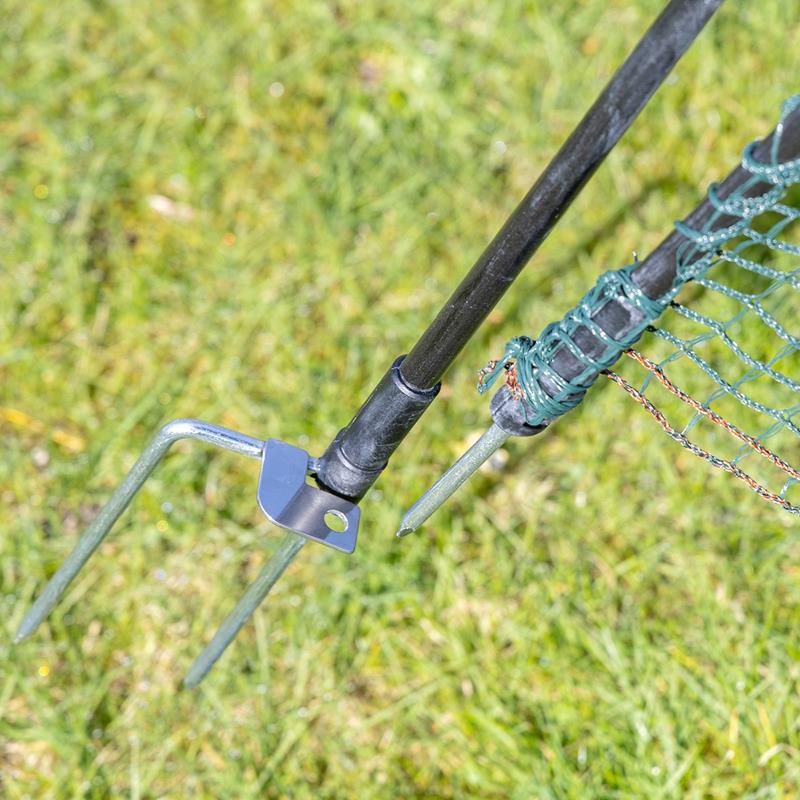 Großansicht der Bildergalerie Nahaufnahme eines VOSS.farming Metall-Erdspießes, der den Mast der "Tür für Weidezaunnetze, ohne Strom, 120cm" auf grünem Gras sichert.